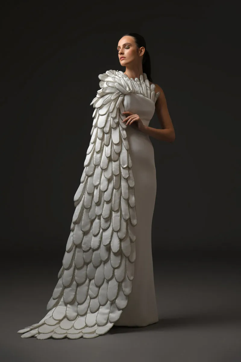 A sculpted gown in white silk scuba paired with layers of 3D hand-crafted plumes emerging from the bust into a cape