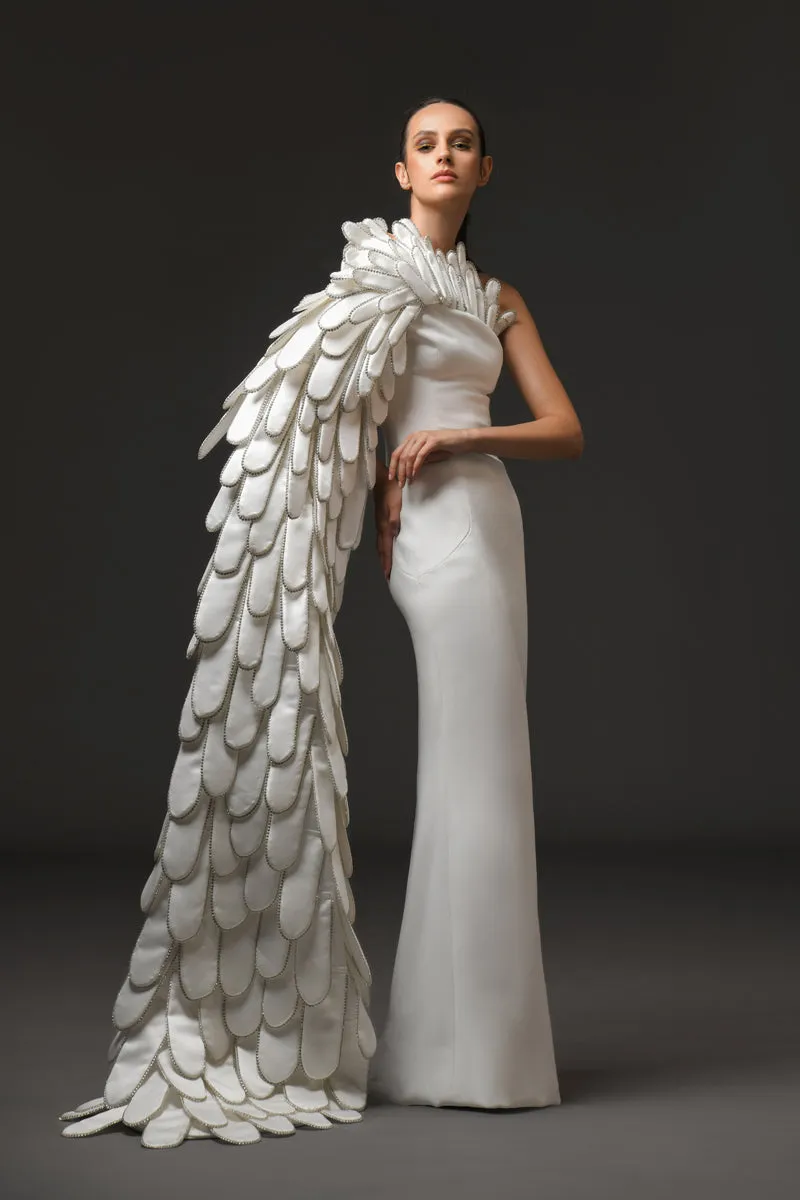 A sculpted gown in white silk scuba paired with layers of 3D hand-crafted plumes emerging from the bust into a cape